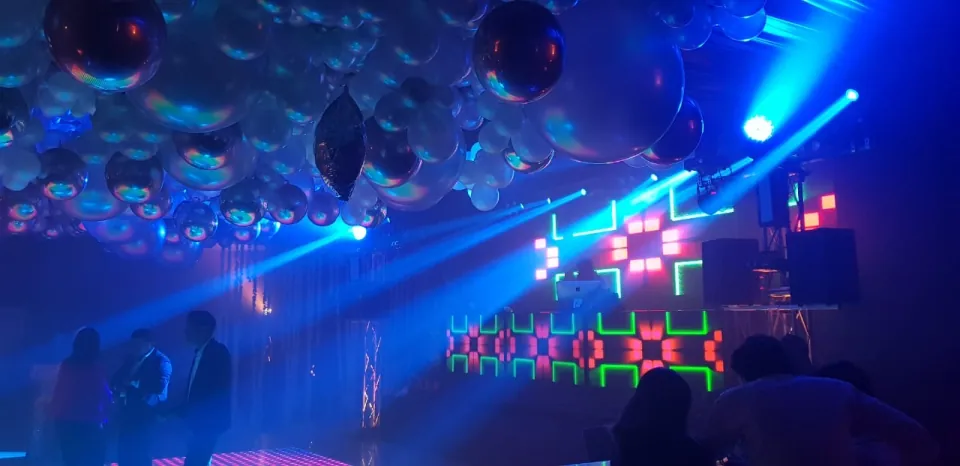 Salón iluminado en azul con esferas suspendidas y una cabina de paneles luminosos.