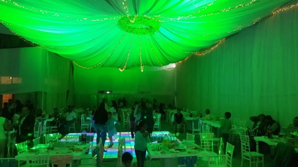 Mesas de un evento bajo telas de techo iluminadas en verde.