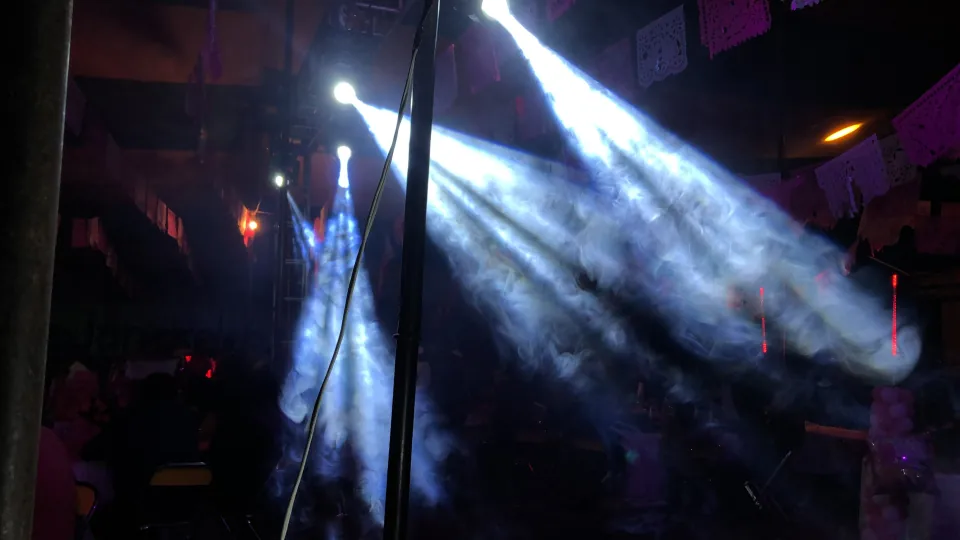 Haces de luz blanca cruzando un montaje de iluminación entre humo escénico.