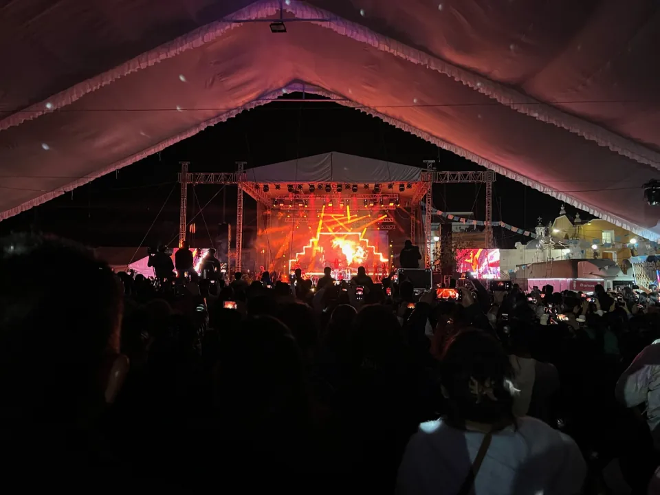 Vista del público y de un escenario iluminado en rojo bajo una carpa.